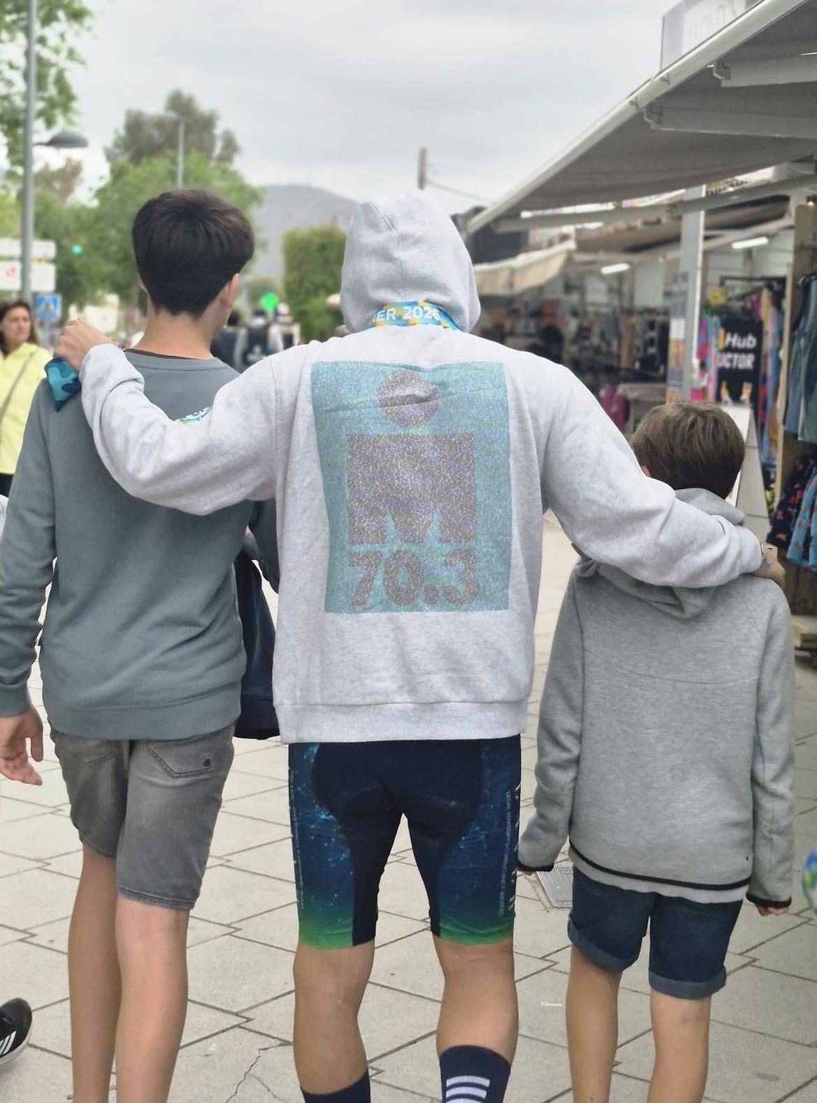 Marc de espaldas, con la sudadera del Ironman 70.3, abrazando a sus dos hijos